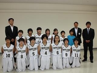 バスケットボールのユニフォームを着た子供数人、スーツを着た大人二人、教育長が記念撮影をした写真。