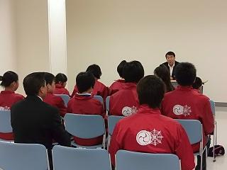 制服を着た学生数人と保護者が、机を挟んで教育長の話を聞いている写真。