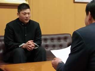 教育長室で椅子を座る橋本さんと表彰する市の男性の写真