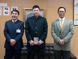 教育長室内で立つ橋本さんと二人のスーツの男性の写真