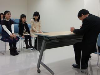スーツを着た男性と机を挟んで、3人の女子生徒が座っている写真