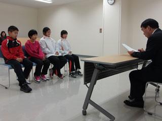 スーツを着た男性と机を挟んで、4人の生徒が座っている写真