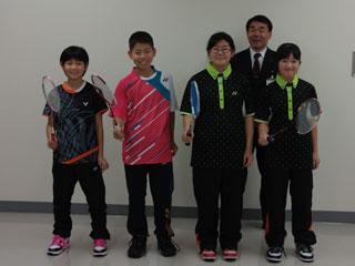 右から、2人の黒いユニフォームを着た生徒と、ピンク色のユニフォームを着た生徒と、黒いユニフォームを着た生徒が並び、後ろにスーツを着た男性が立っている写真