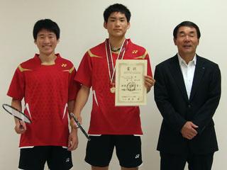 右から、スーツを着た男性と、2人の赤いユニフォームを着た男子生徒が並んでいる写真