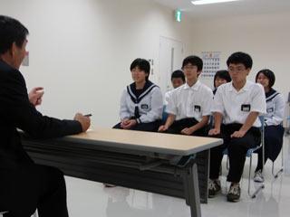 スーツを着た男性と机を挟んで、制服を着た複数の生徒が座っている写真