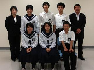6人の制服を着た生徒が2列に並び、その両隣にスーツを着た方が立っている写真