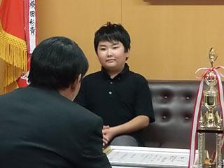 スーツを着た男性と机を挟んで、黒い服を着た生徒が座っている写真