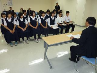 スーツを着た男性と机を挟んで、複数の制服を着た生徒が座っている写真