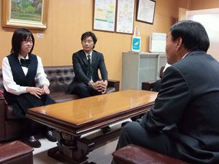 スーツを着た男性と机を挟んで、スーツを着た男性と、制服を着た女子生徒が座っている写真