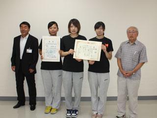 左からスーツを着た男性と、3人の賞状を持った女子選手と1人の男性が並んでいる写真