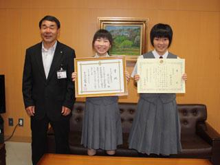 左からスーツを着た男性と、2人の制服を着て賞状を持っている女子生徒が並んでいる写真