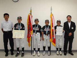 左からワイシャツを着た男性と、4人のユニフォームを着た男子生徒と、その右にスーツを着た男性が並んでいる写真