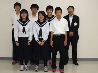 前列、左から制服を着た2人の女子生徒と1人の男子生徒が立って並んでいて、後列、左から制服を着た2人の男子生徒と1人の女子生徒、スーツを着た男性が並んで立っている写真