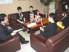 トロフィーの置かれた机の周りで談笑する教育長と学生たちの写真