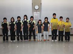 室内で、ユニフォーム姿のラケットを持った学生男女10名が横一列に並んで立っている写真