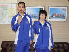 応接室で、青いジャージ姿の男子学生1名と女子学生1名が、片手を持ち上げガッツポーズをしている写真
