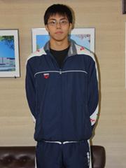 後ろで手を組みながらカメラ目線で正面を見て立っている紺と白のジャージ姿の選手の写真