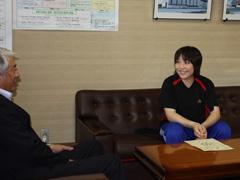 椅子に座り、笑顔で市長の話を聞く水間里美さんの写真