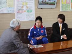 青いジャージ姿の選手と黒いスーツ姿の男性が教育委員会を訪問している写真