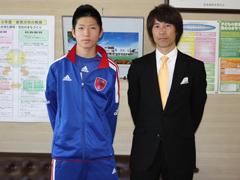 青いジャージ姿の選手と黒いスーツ姿の男性のツーショット写真