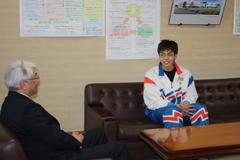 白いジャージ姿の選手がスーツ姿の教育委員会の担当者と談笑している写真