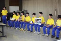 黄色いシャツに青いジャージの選手団が教育委員会を訪問している写真