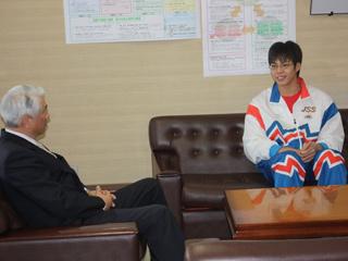 白いジャージ姿の選手がスーツ姿の教育委員会の担当者と談笑している写真