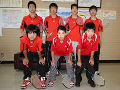 二列に分かれてユニフォーム姿でバドミントンラケットを持って記念撮影する学生の写真