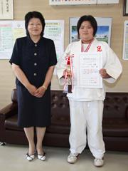 柔道着姿で賞状とトロフィーを持って記念撮影する女子生徒の写真