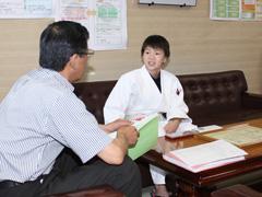 室内で道着姿の小学生がソファに座りながら机向かいに教育長と対談している写真