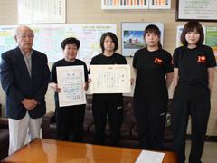 室内で黒Tシャツ姿の高校生と顧問達が賞状を両手で持って教育長と並んで撮影されている写真