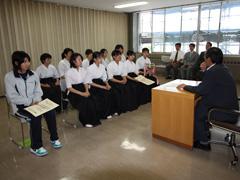 弓道着姿の女子学生達が椅子に座り、教育長が子どもたちへ奨励している様子の写真