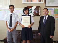 制服姿の女子学生が賞状を両手で持って顧問と並んで撮影されている写真