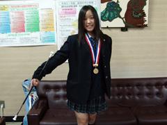 メダルを首からかけバトンを使いポーズを取る女子学生の写真