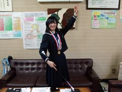 メダルを首からかけバトンを使いながら手を上げポーズを取る女子学生の写真