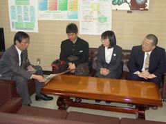 書状を読む教育長の前に座る男子学生と大人二人の写真