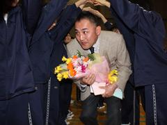 花束を持った男性が生徒たちの花道を潜り抜ける写真
