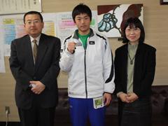 真ん中にジャージ姿の選手と、左隣にスーツ姿の男性、右隣に女性が写っている写真