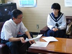 ワイシャツを着た男性と机を挟んで、制服を着た女子生徒が椅子に座っている写真