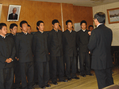 制服を着た男子生徒達と、スーツを着た男性が向かい合って立っている写真
