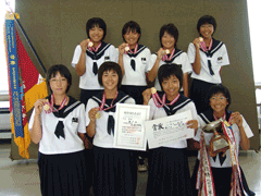 首から赤い紐の付いたメダルをぶら下げて賞状やトロフィーを持っている光陵中学校女子ソフトテニス部の女子生徒の写真