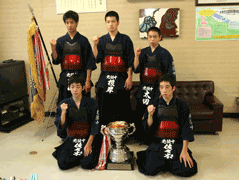 優勝トロフィーを囲むように剣道着を着ている岩見沢鉄北少年剣道教室の皆さんの集合写真