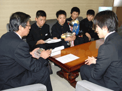 岩見沢市の教育長を訪問し、ソファに腰かけて教育長の話を聞いている千葉 亮輔さん、上村 昇平さん、永野 晶暉さん、黒瀬 雅人さんが映っている写真