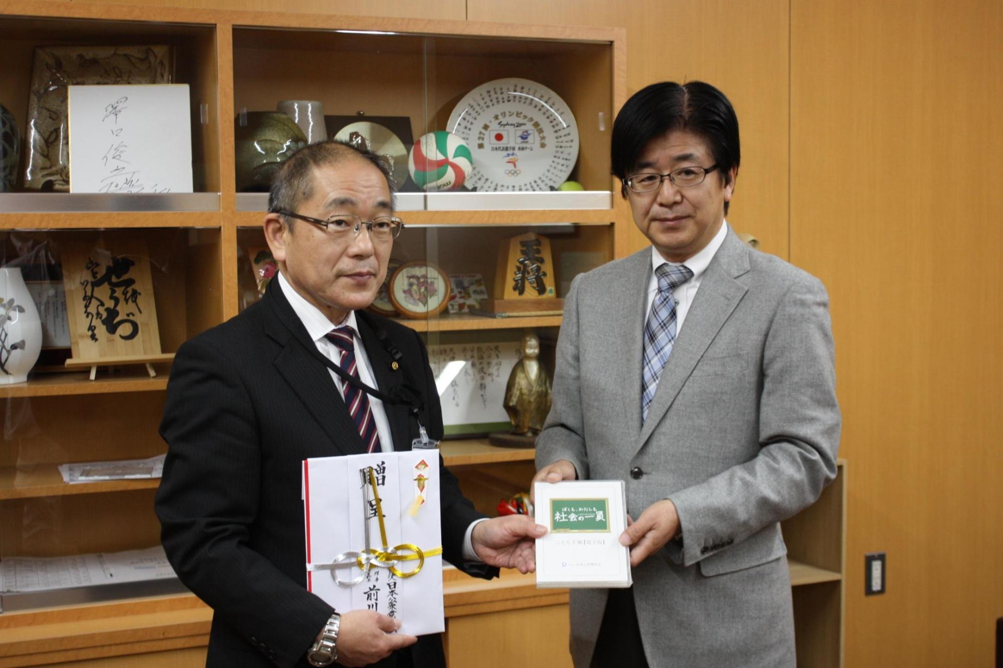 眼鏡をかけた二人の男性が贈呈と書かれたのしと書物を持っている写真