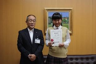 右に制服を着た女子生徒が立って、賞状をこちらに向けており、左にスーツを着た男性が立って並んでいる写真