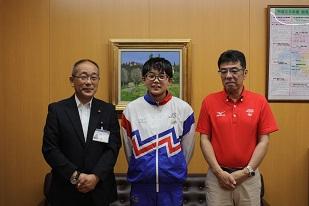 右から、赤い服を着た男性と、ユニフォームを着た男子生徒と、スーツを着た男性が並んでいる写真