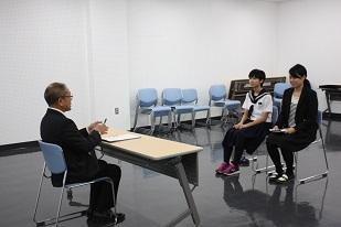 椅子に座って教育長の話を聞く制服姿の女子生徒の写真