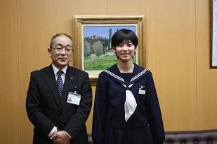木壁と絵画が飾ってある室内で教育長と学生服の女学生が並んで撮影された写真