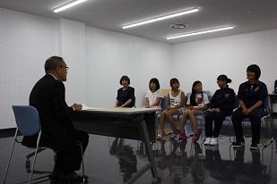 スーツを着た男性と机を挟んで、5人の女子生徒と、1人の女性が椅子に座っている写真