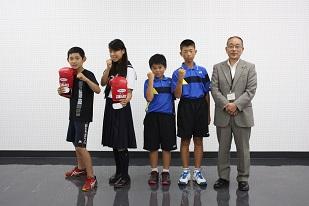 右からスーツを着た男性と、2人の青いユニフォームを着た男子生徒と、制服を着た女子生徒と、黒いユニフォームを着た男子生徒が並んでいる写真